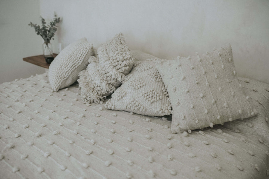 set of handmade wool pillows on neutral quilt bed